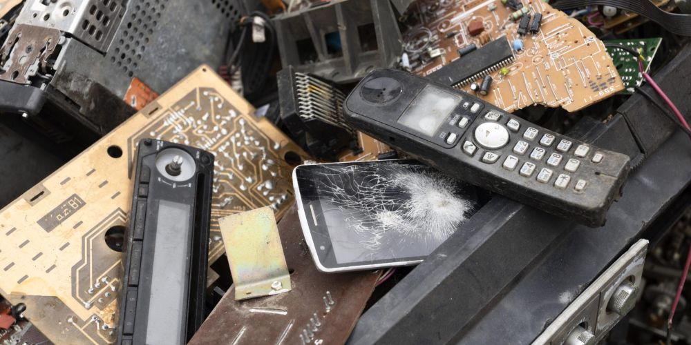 Hromada rôzneho elektronického odpadu a starých spotrebičov, ako sú telefóny a obvodové dosky, symbolizujúca komplexnosť problematiky elektroodpadu a kľúčové povinnosti Rozšírenej Zodpovednosti Výrobcov (RZV) pre elektrozariadenia, batérie a akumulátory.